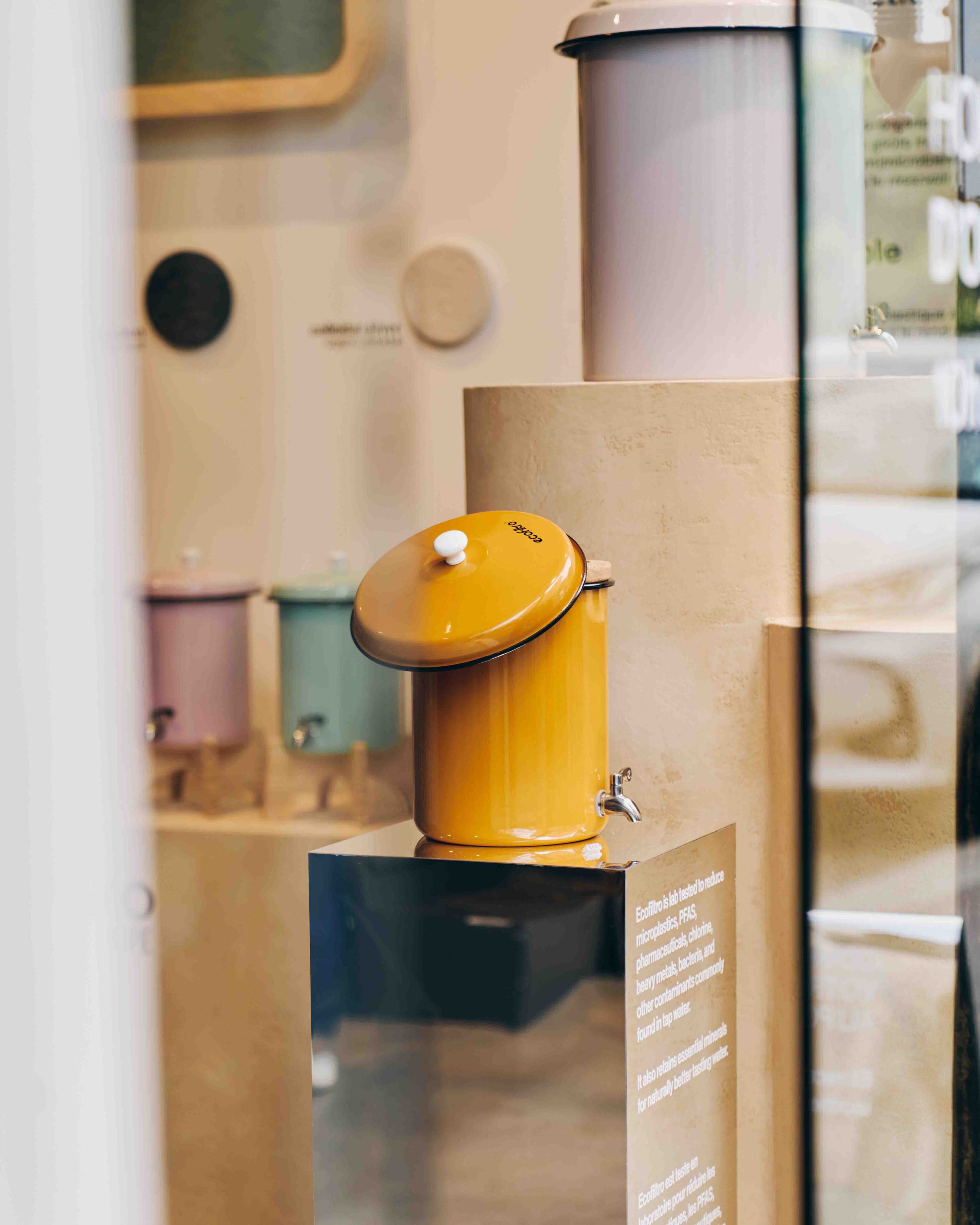 Yellow Ecofiltro dispenser on mirrored base, lid askew.