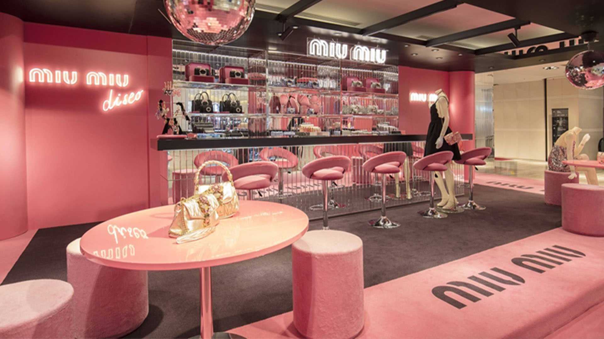 Inside Miu Miu Disco pop-up, pink decor, bar, neons, disco balls, bags.