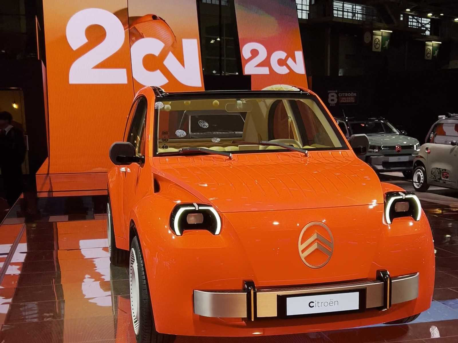 Front view of the orange 2CV in front of the “2CV” screens on the Citroën booth