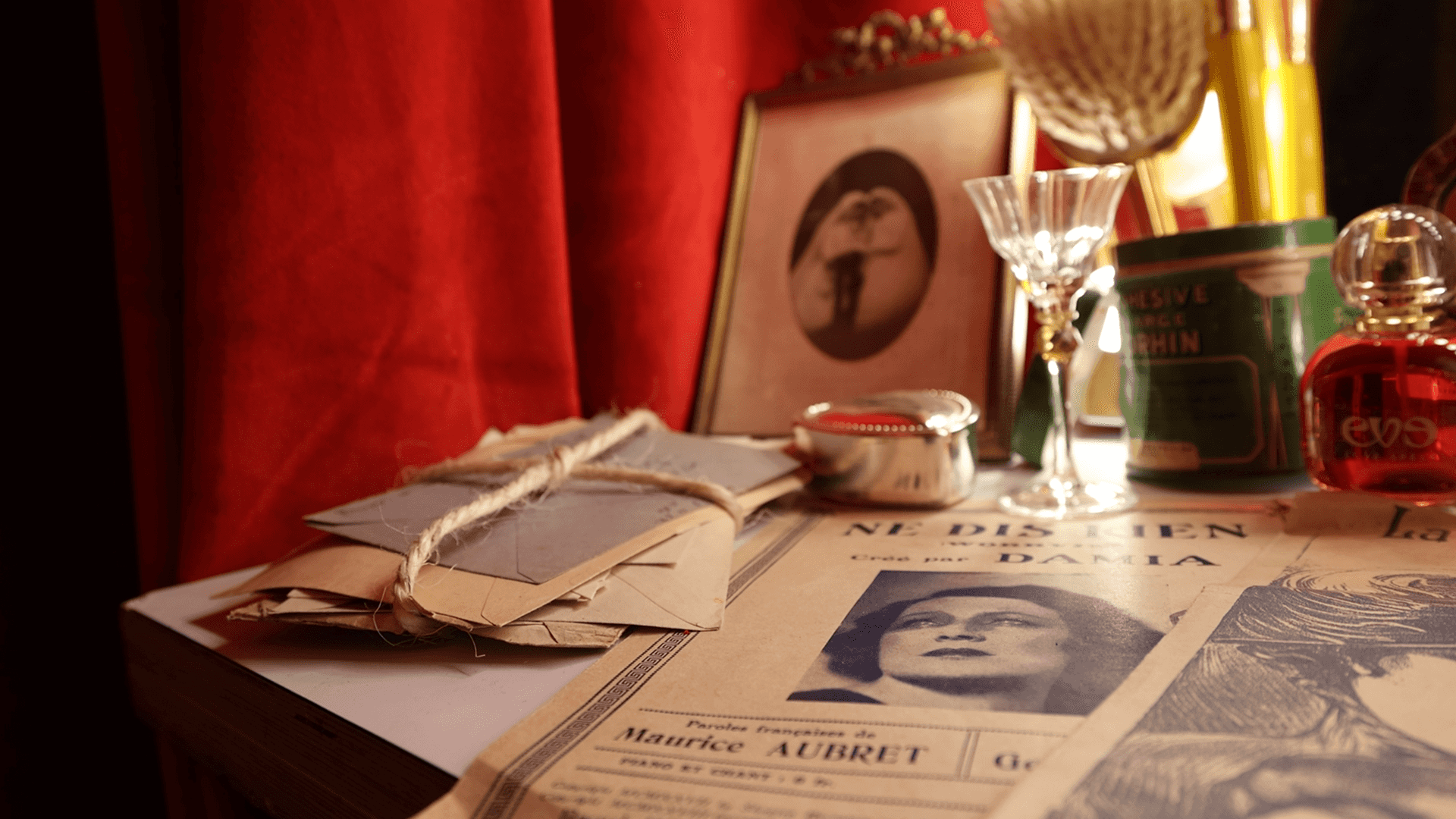 Vintage letters, Damia sheet music, red velvet curtains, cabaret decor.